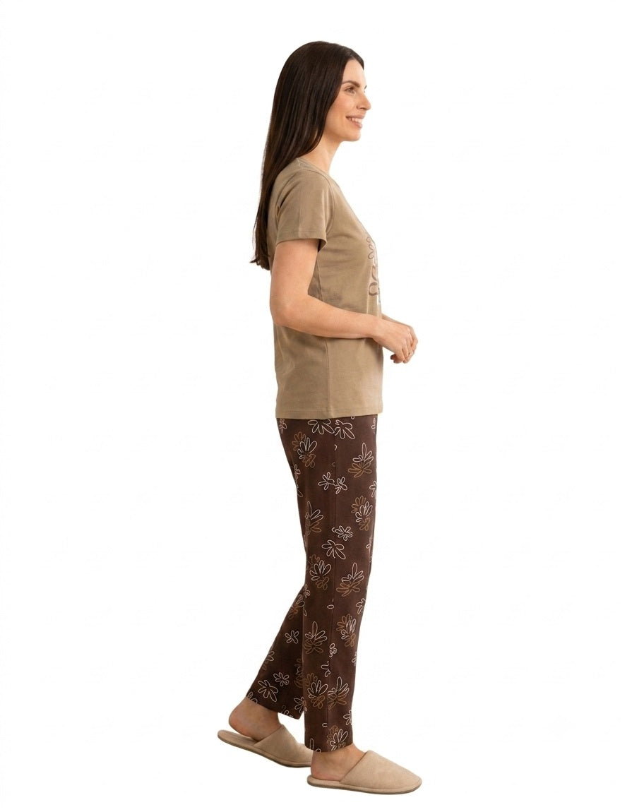 A woman shown in side profile wearing a two-piece pajama set consisting of a short-sleeve honey color top and brown pants with a light beige floral pattern, against a plain white background.