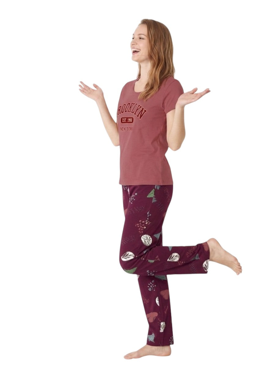 A woman modeling a two-piece pajama set consisting of a dusty pink short-sleeve t-shirt with a graphic print and purple patterned pants, posed against a solid white background.