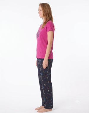 A woman modeling a two-piece pajama set consisting of a toffee pink short-sleeve t-shirt with a dark blue circular graphic and matching navy pants with a colorful pattern, set against a plain white background.