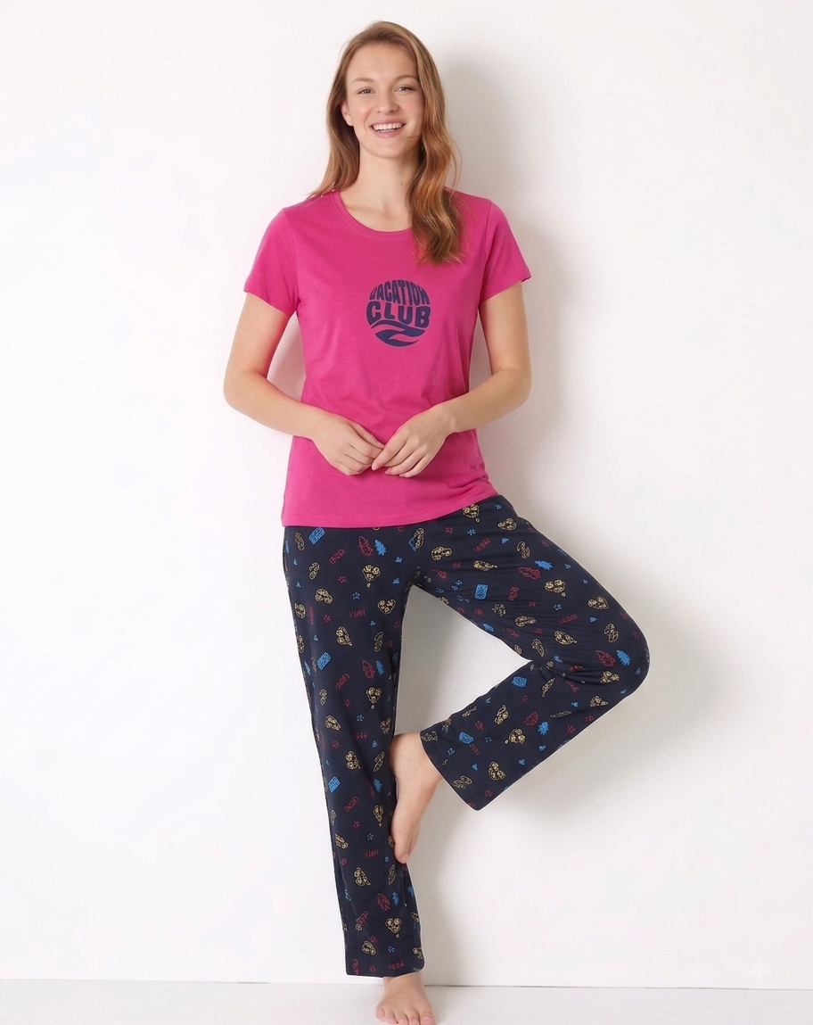 A woman modeling a two-piece pajama set consisting of a toffee pink short-sleeve t-shirt with a dark blue circular graphic and matching navy pants with a colorful pattern, set against a plain white background.
